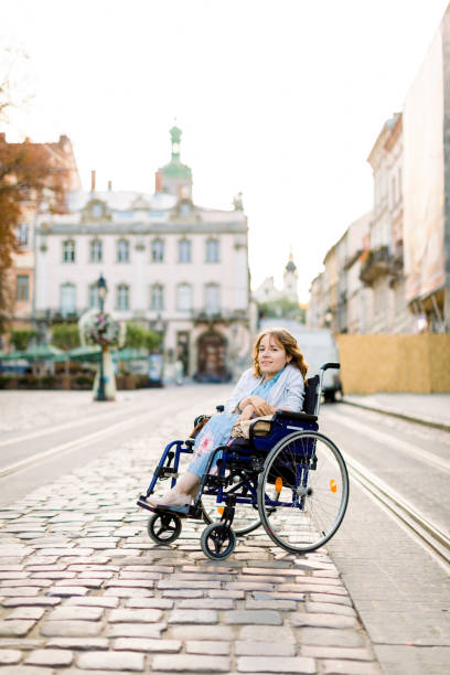 beautiful disabled woman in wheelchair smiling at camera while walking in the old city center - wheelchair street happy imagens e fotografias de stock