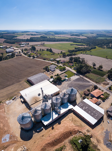 Beautiful drone aerial view of agricultural silos to store soy and corn on farm in Brazil. Concept of agriculture, economy, rural landscape, technology, business. Metal roofs o sunny summer day.