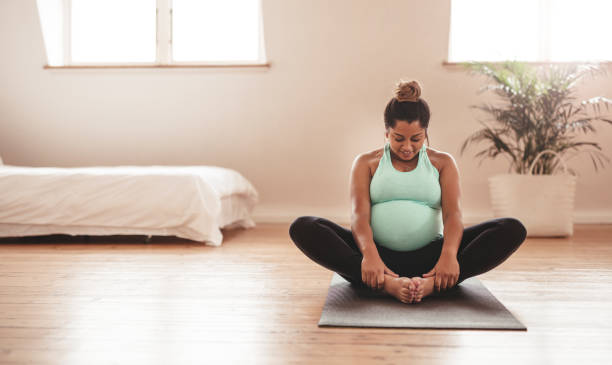 Beautiful expectant mother doing yoga at home Portrait of young pregnant female working out at home. African pregnant woman practicing yoga at home. Prenatal groins stretch. Buddha Konasana Pose. Pregnancy yoga and fitness. healthy habits during pregnancy stock pictures, royalty-free photos & images