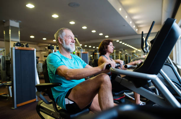 Beautiful fit senior couple in gym doing cardio work out. Beautiful fit senior couple in sports clothing in gym doing cardio workout, exercising on recumbent bicycle. Sport fitness and healthy lifestyle concept. recumbent bike gym stock pictures, royalty-free photos & images