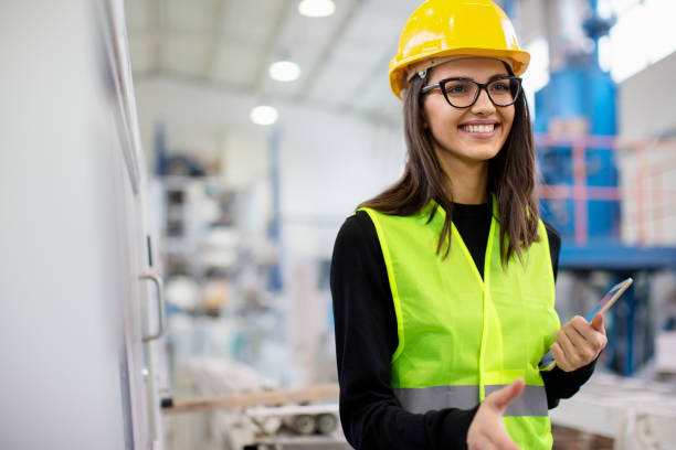 Beautiful girl at factory in a vest and helmet smiling going for a handshake stock photo