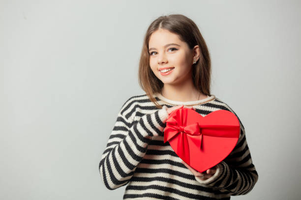 Beautiful girl in striped sweater with heart shape gift box on white background stock photo