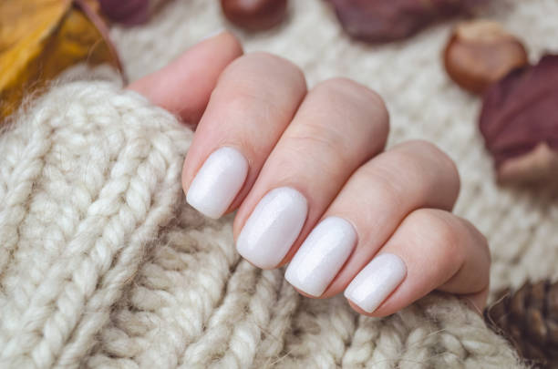 Beautiful hand of a young woman with a knitted sweater and autumn leaves. The nails are covered with a white gel Polish with a shimmer. Manicure ideas. Beautiful hand of a young woman with a knitted sweater and autumn leaves. The nails are covered with a white gel Polish with a shimmer. Manicure ideas. artificial nail stock pictures, royalty-free photos & images