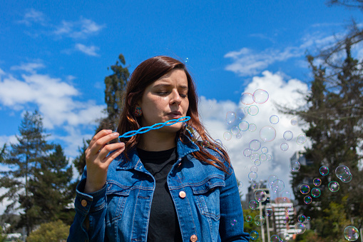 Portrait of beautiful Hispanic woman blowing soap bubbles in the middle of a park on a sunny morning