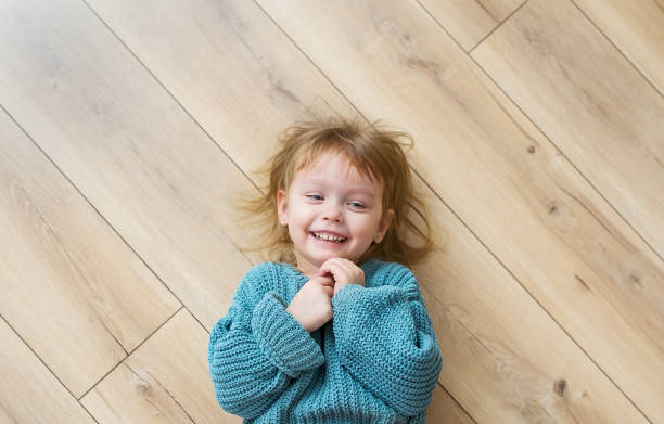 bella bambina gioiosa in maglione blu si trova sul pavimento in legno. visualizzazione dall'alto - floor top view foto e immagini stock