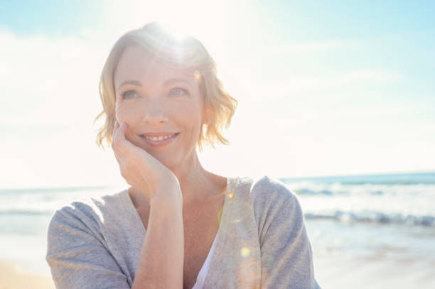 Beautiful mature woman portrait on the beach. Beautiful mature woman portrait on the beach. She is happy and smiling with the sun and sea behind her. She looks relaxed and could be on vacation. good looking older women pictures stock pictures, royalty-free photos & images