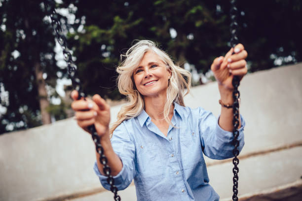 Beautiful mature woman sitting on swing and having fun Happy senior woman with gray hair having fun at playground sitting on swing wundervisuals stock pictures, royalty-free photos & images