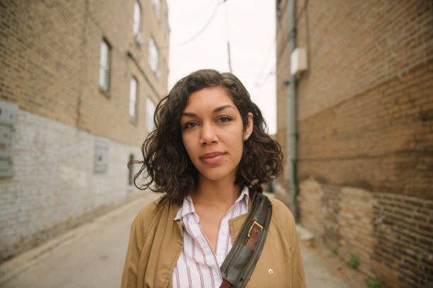 Beautiful Millennial Puerto Rican Woman in Urban Chicago Neighborhood USA This is a horizontal, color portrait of a beautiful, smiling Hispanic Puerto Rican woman walking through a brick lined alley in a residential, urban neighborhood of Chicago, Illinois. She looks at the camera wearing a light brown jacket and a brown messenger bag on an overcast, autumn as she walks to work. puerto rican women stock pictures, royalty-free photos & images