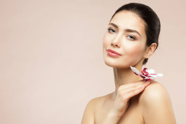 Beautiful Model Girl holding Orchid Flower on Shoulder. Beauty Woman with Perfect Healthy Skin and Natural Makeup. Body and Face Care Cosmetics stock photo