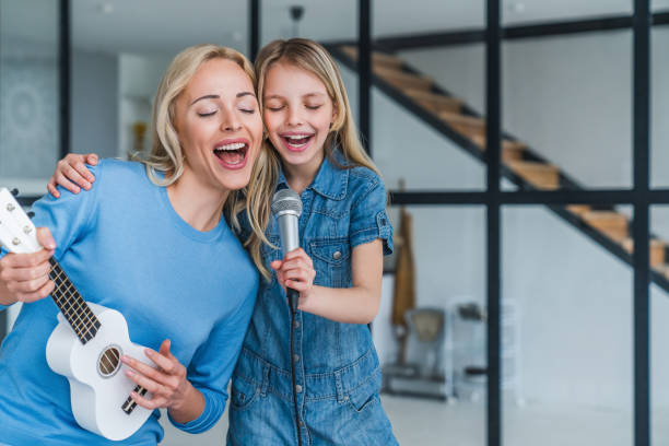 Beautiful mother and her cute little daughter with microphone singing together and playing ukulele Child, People, Females, Parent, Happiness singing stock pictures, royalty-free photos & images