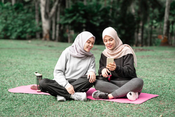 Beautiful muslim ladies sitting down and technology lifestyle concept at a public park during a sunny day after doing some exercise stock photo