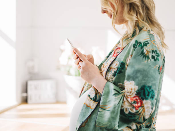 Beautiful pregnant woman with smart phone in the kitchen stock photo