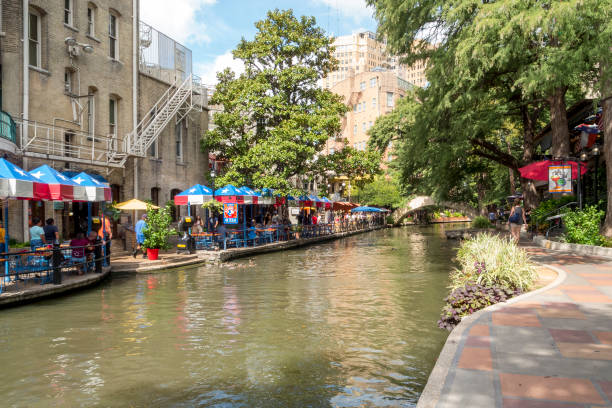 Beautiful San Antonio Riverwalk in Early Fall This view shows some of the scenery along the famous San Antonio Riverwalk in the heart of the Texas city.  This picture was taken in the early fall while the temperatures were still very hot.  Bright umbrellas lining one side of the riverbank can be seen in this shot. has san hawkins stock pictures, royalty-free photos & images