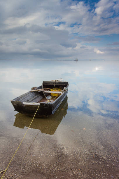 Beautiful seascape with a single boat reflected in the still ocean at sunrise stock photo