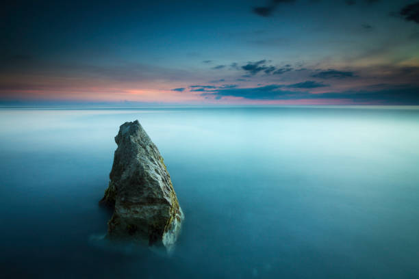 Beautiful seascape with a single rock leading out to the sunset stock photo