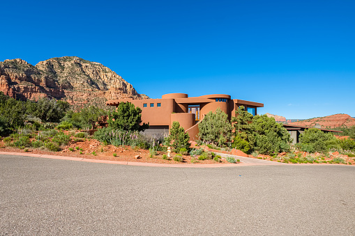 Sedona, Arizona USA - April 25, 2017: Typical modern adobe style architecture desert home with majestic red rock formations in the background in this popular tourist destination.