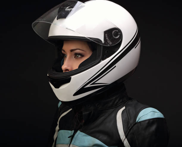 Beautiful serious makeup profile of rider woman looking in white motorcycle helmet and leather fashion protective jacket on black background. Closeup dark portrait of biker female stock photo