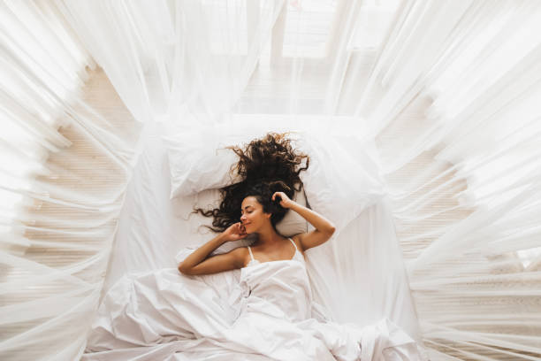 Beautiful smiling girl awakening in white bed. Happy wake up and start new day. Leisure and rest. View from above. Wellbeing concept. stock photo