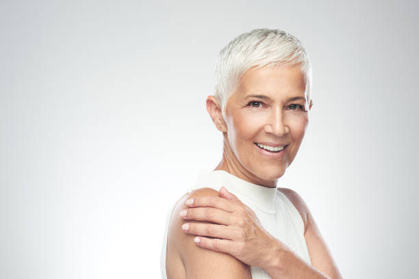 vacker leende senior kvinna med kort grått hår poserar framför grå bakgrund. skönhetsfotografering. - medelålders kvinnor bildbanksfoton och bilder