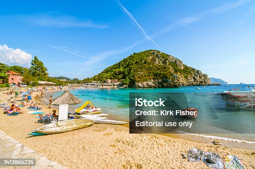 A beautiful summer day at Paleokastritsa beach, with shops and cafes in the village and boats in view on a summer day as tourists enjoy the sandy beach on the island of Corfu, Greece.