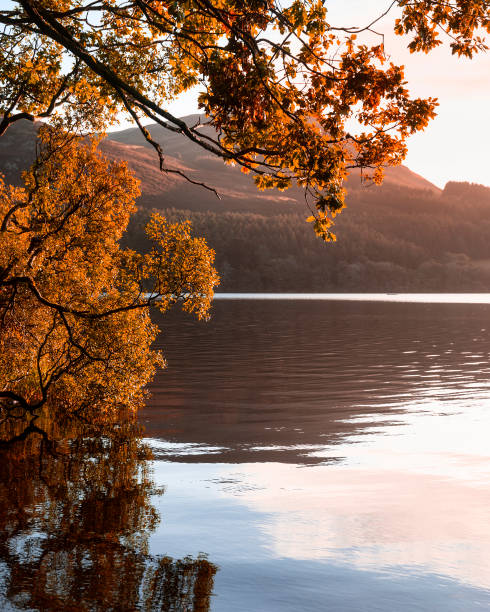Beautiful sunrise landscape image looking across Loweswater in the Lake District towards Low Fell and Grasmere with vibrant sunrise sky breaking on the mountain peaks stock photo