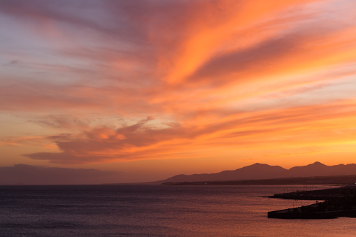 wonderful sunset on the beach, the golden light of the sun dyes the clouds orange and pink, with mountains in the background. Lanzarote, Canary Islands, Spain