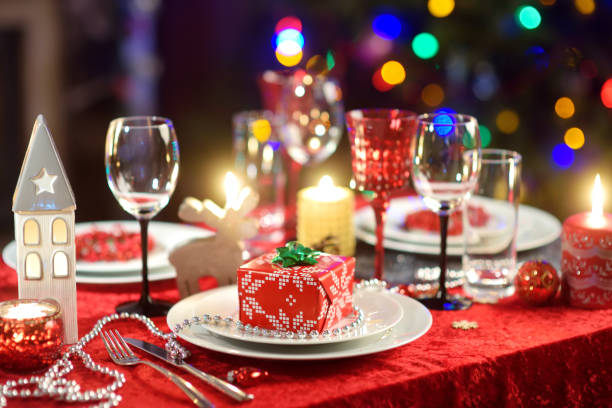 Beautiful table setting for Christmas party or New Year celebration at home. Cozy room with a fireplace and Christmas tree in a background. stock photo