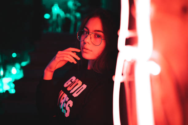 Beautiful teenage girl standing next to neon light at night stock photo