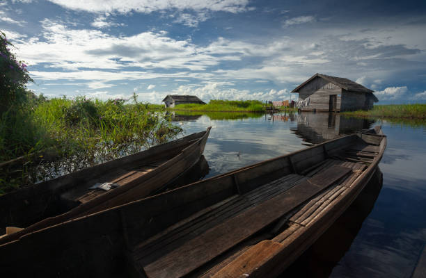 beautiful view of a calm lake with wooden boats and houses surrounded by grass stock photo