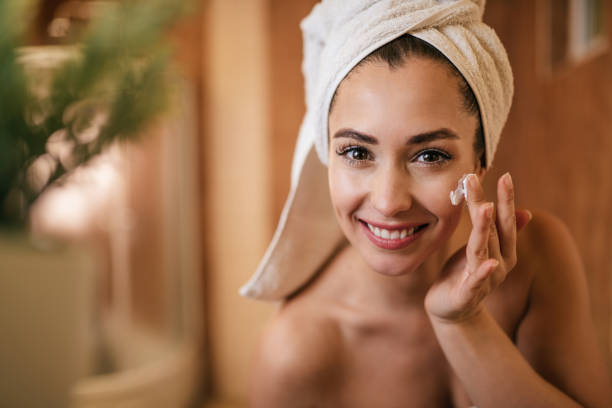 Beautiful woman applying moisturizer on her face in the bathroom. Young beautiful woman applying face cream in the bathroom. applying face cream stock pictures, royalty-free photos & images