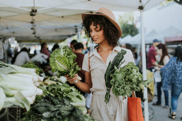 hermosa mujer compra kale en un mercado - farmers market fotografías e imágenes de stock