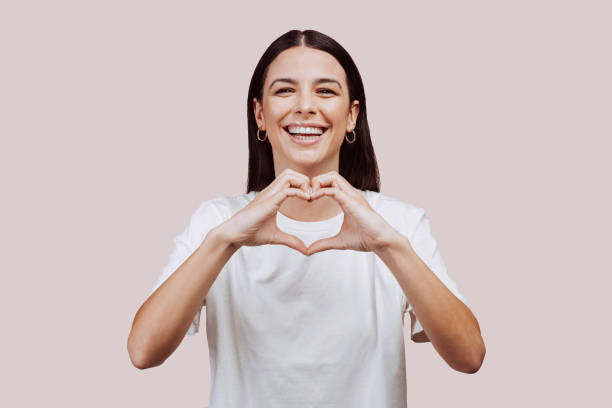 Beautiful woman doing love hearth sign with hands at studio stock photo