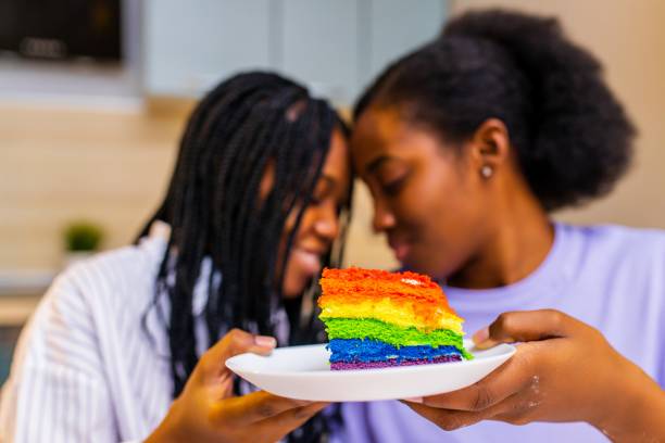 Beautiful woman feeding her wife with rainbow colorful cake and celebrating anniversary or Valentine stock photo