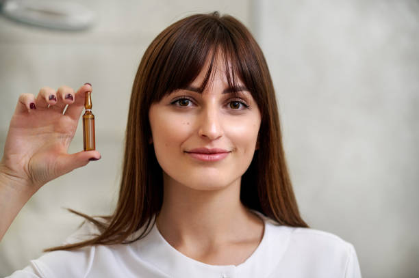 A beautiful woman holding ampoule at the level of her face A beautiful woman holds an ampula of dark glass at the level of her face ampoule stock pictures, royalty-free photos & images