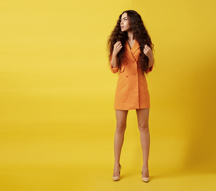 Beautiful woman in orange jacket standing front of yellow background.