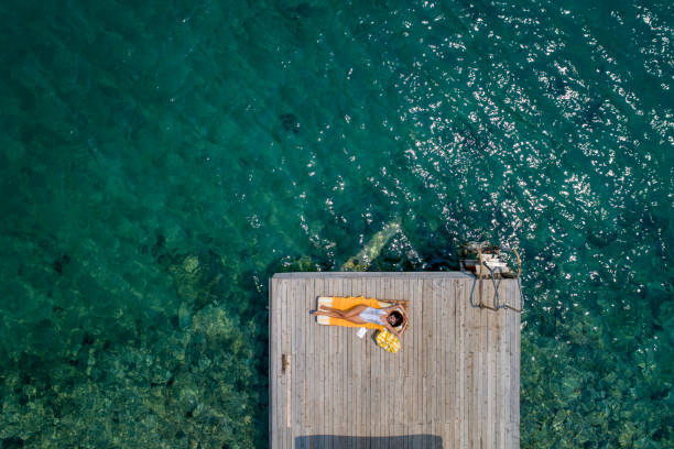 Beautiful woman sunbathing alone on a wooden pier in sea aerial photo stock photo