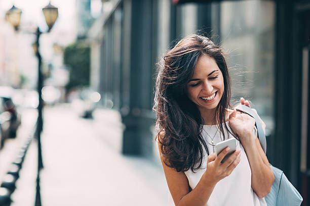 Beautiful woman texting on the street Smiling young woman walking outdoors at urban setting and checking messages. beautiful woman smiling stock pictures, royalty-free photos & images