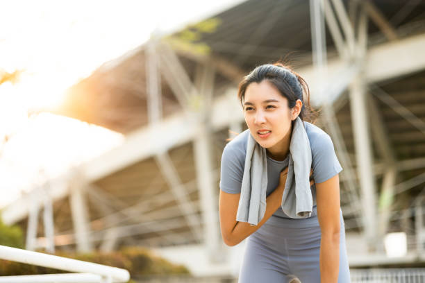 Beautiful woman tired during jogging in the city at sunrise. Young asian female intense training workout challenge breathing exhausted. Exercise in the morning. Healthy and active lifestyle concept. stock photo
