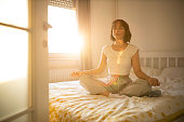 istock Beautiful woman waking up in her bed, she practicing yoga. Young beautiful woman waking up in her bed fully rested. Woman exercising yoga in bed after wake up. 1290872883