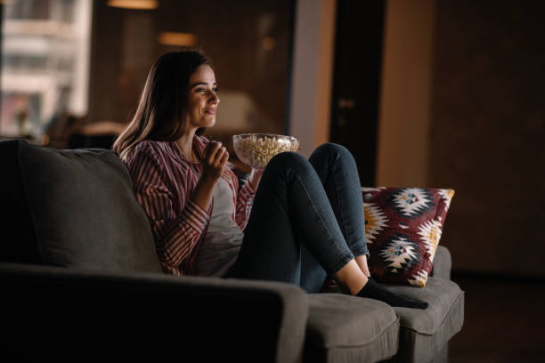 Beautiful woman watching movie in the night sitting on a couch in the living room at home stock photo