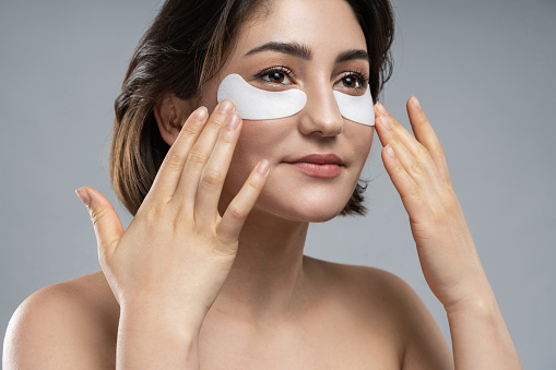 Beautiful brunette woman with a smooth skin applying adhesive under-eyes patches for dark circles