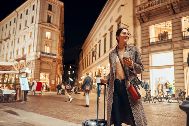 belle femme avec une valise dans la ville utilisant son téléphone - night lugage photos et images de collection