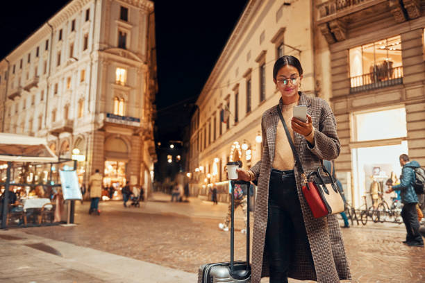 belle femme avec une valise dans la ville utilisant son téléphone - night lugage photos et images de collection