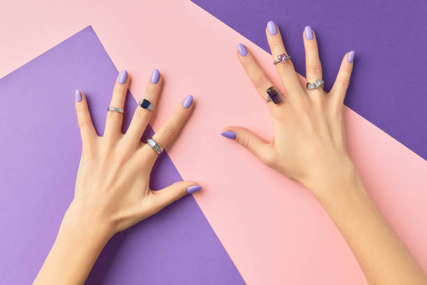 Beautiful womans hands in with purple fashionable spring nail design on pink purple background stock photo