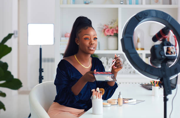 beautiful young african american woman streaming a beauty vlog from home, online content creator applying a makeup on stock photo