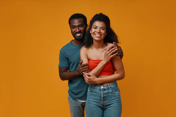Beautiful young African couple smiling and embracing while standing against yellow backgroundbracing stock photo