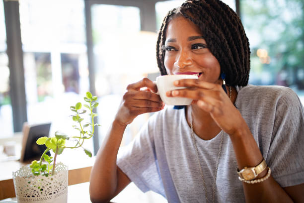 mooie jonge afrikaanse vrouw genieten van een kopje koffie - woman drinking coffee stockfoto's en -beelden