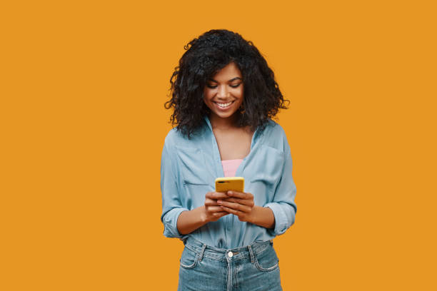 Beautiful young African woman in casual clothing using smart phone and smiling stock photo