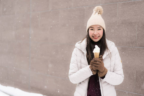 Beautiful young asian woman smile and happy with ice cream in snow winter season stock photo