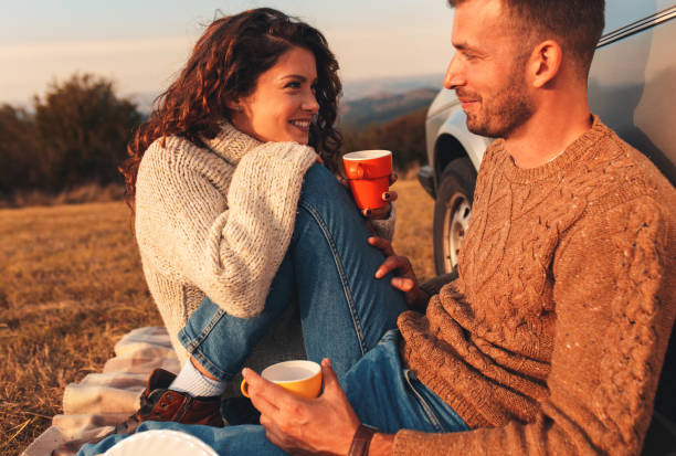 Beautiful young couple enjoying picnic time on the sunset. Beautiful young couple enjoying picnic time on the sunset. They drinking tea and sitting in a meadow leaning against a old fashioned car. dating stock pictures, royalty-free photos & images